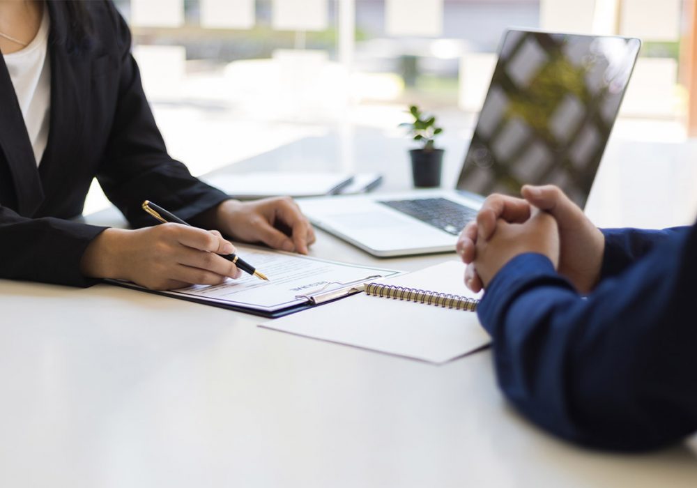 Two people meet at a desk, reviewing documents with a laptop open nearby