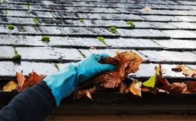 Hand clearing wet leaves from gutter edge.